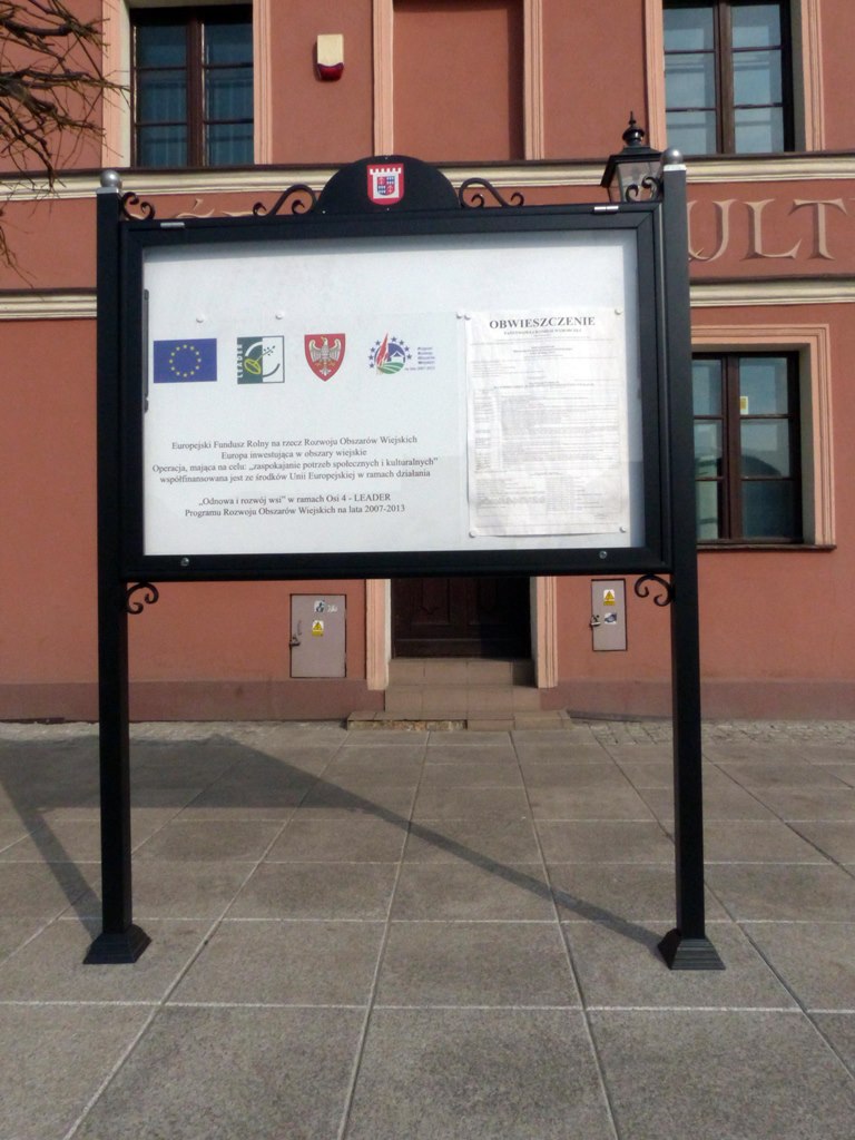 Duża, czarna gablota wolnostojąca z drzwiami jednoskrzydłowymi, zamykana na klucz, przeznaczona do ekspozycji ogłoszeń na zewnątrz.