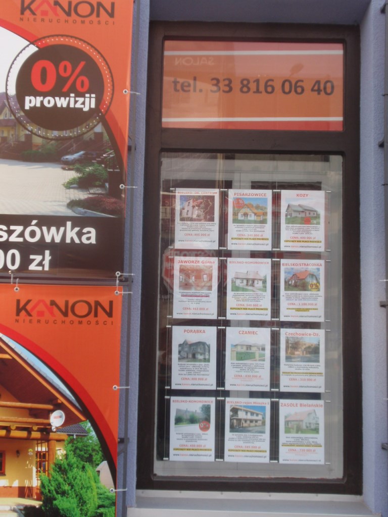Klasyczna witryna biura nieruchomości z papierowymi ofertami prezentowanymi za szybą
