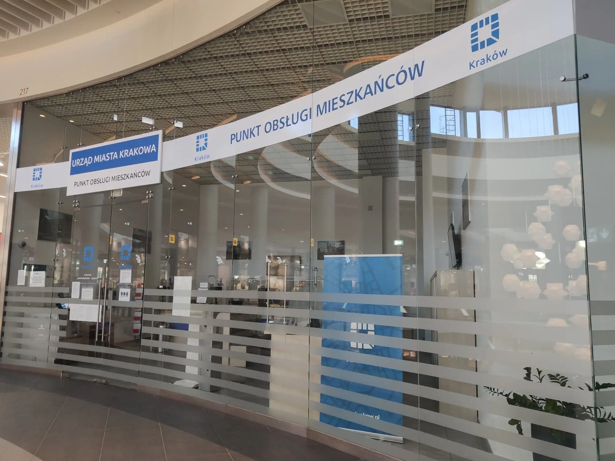 Punkt Obsługi Mieszkańców Urzędu Miasta Krakowa zlokalizowany w nowoczesnym, przeszklonym lokalu. Czytelne oznakowanie ułatwia dostęp do usług administracyjnych.
